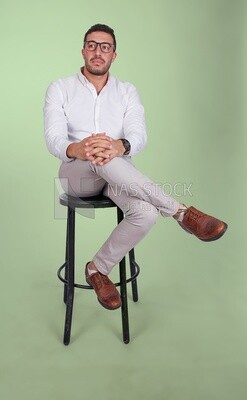 Photo of a Handsome man sitting on a chair and putting a leg on a leg, Smiling Man, Wearing formal Clothes Posing In a Light Room Interior, Smiling At the Camera