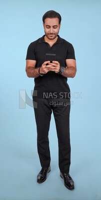 Photo Of a Handsome man Standing and holding his mobile, Smiling Man, Wearing Casual Clothes Posing In a Light Room Interior, Smiling At the Camera