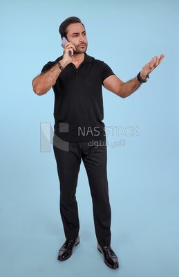 Portrait of a handsome man standing and talking to the mobile phone looking annoyed, man smiling, dressed in casual clothes in light room interior, smiling at camera