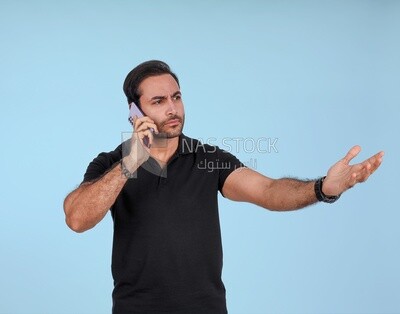 Portrait of a handsome man standing and talking to the mobile phone looking annoyed, man smiling, dressed in casual clothes in light room interior, smiling at camera