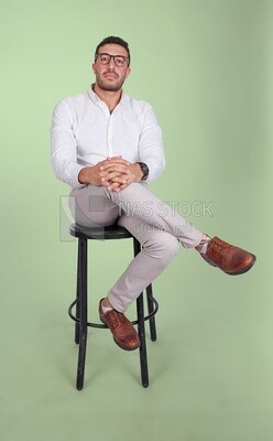 Photo of a Handsome man sitting on a chair and putting a leg on a leg, Smiling Man, Wearing formal Clothes Posing In a Light Room Interior, Smiling At the Camera