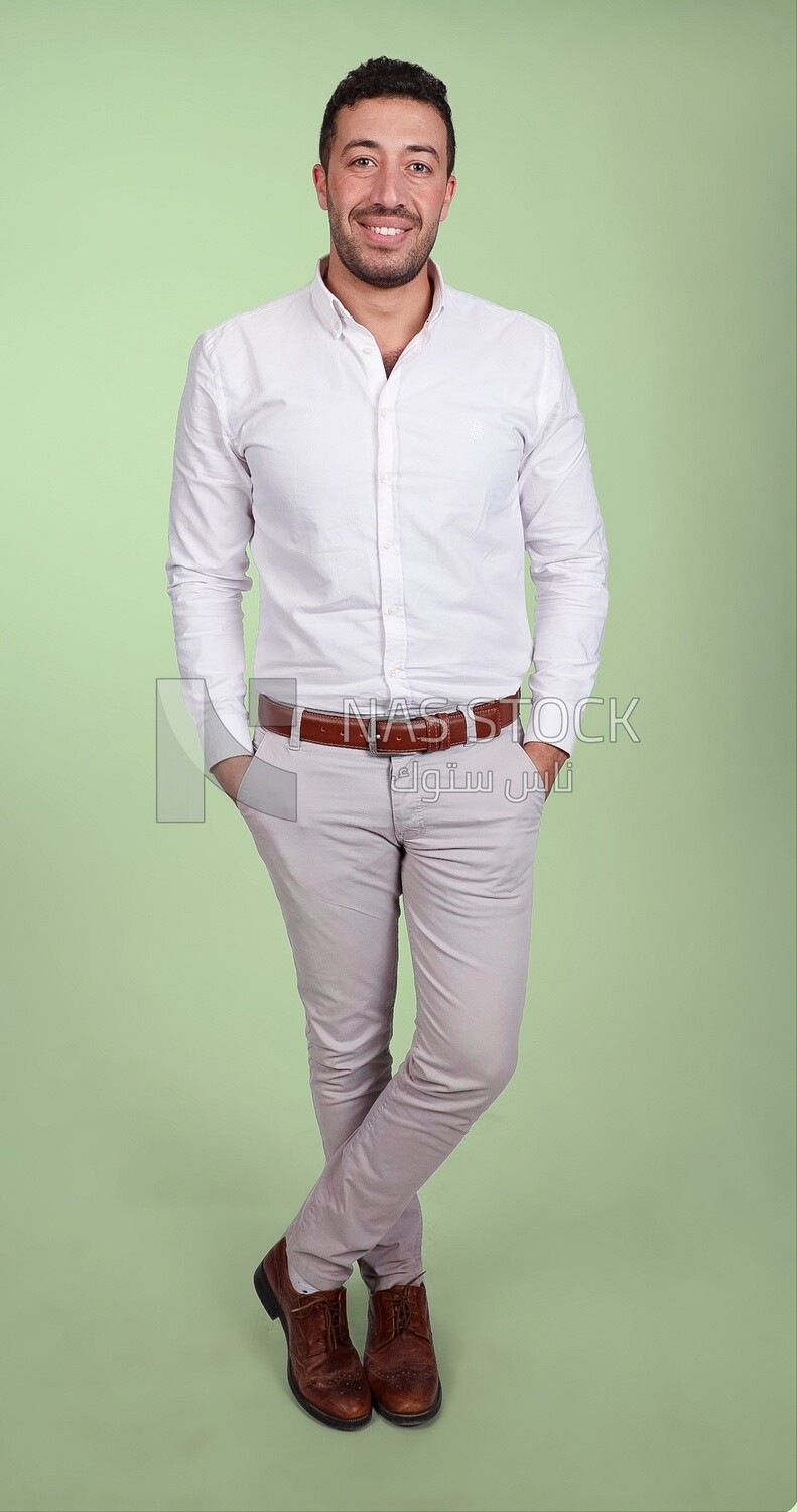 Photo of a handsome man standing and putting his hand in his pocket, a smiling man, dressed casually in an indoor light room, smiling at the camera, looking away