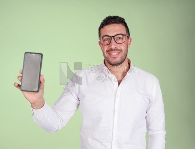 Photo of a Handsome man Standing and holding his mobile, Smiling Man, Wearing formal Clothes Posing In a Light Room Interior, Smiling At the Camera