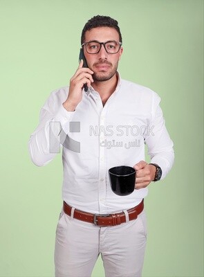 Photo of a handsome man wearing glasses standing talking on his phone and drinking coffee, business development and partnerships, business meeting, model