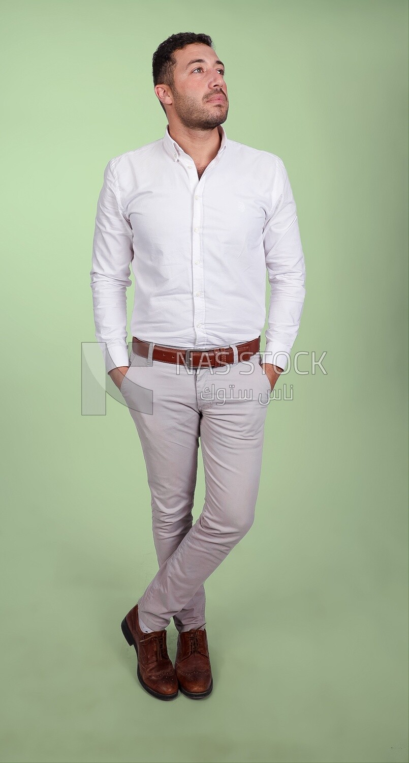 Photo of a handsome man standing and putting his hand in his pocket, a smiling man, dressed casually in an indoor light room, smiling at the camera, looking away
