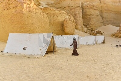 A scene of a Bedouin man standing next to tents among the mountains in Wadi El Hitan, Egypt
