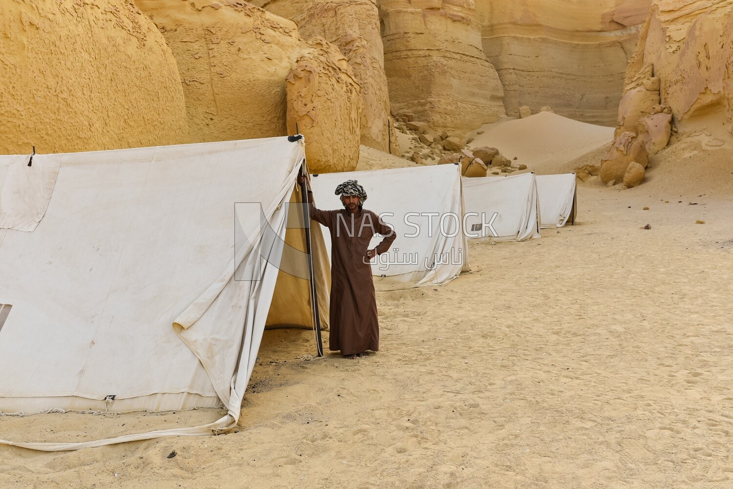 A scene of a Bedouin man standing next to tents among the mountains in Wadi El Hitan, Egypt