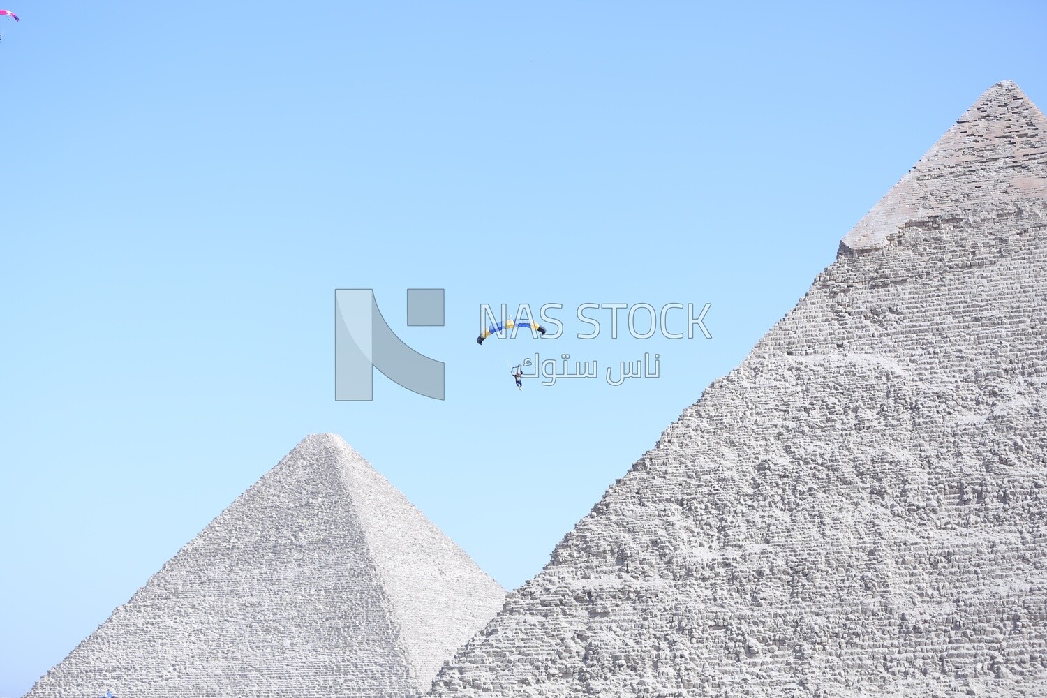 Scene of a person flying in the sky wearing a parachute in front of the Egyptian pyramids