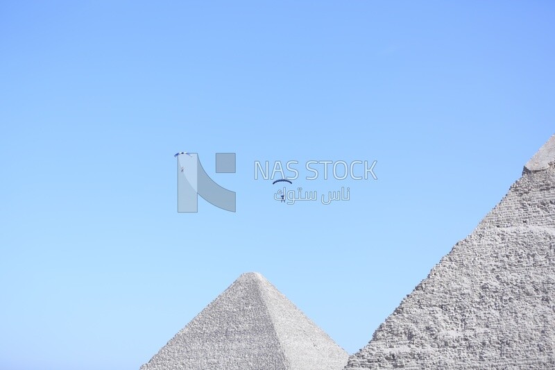 People flying in the sky wearing a parachutes in front of the Egyptian pyramids