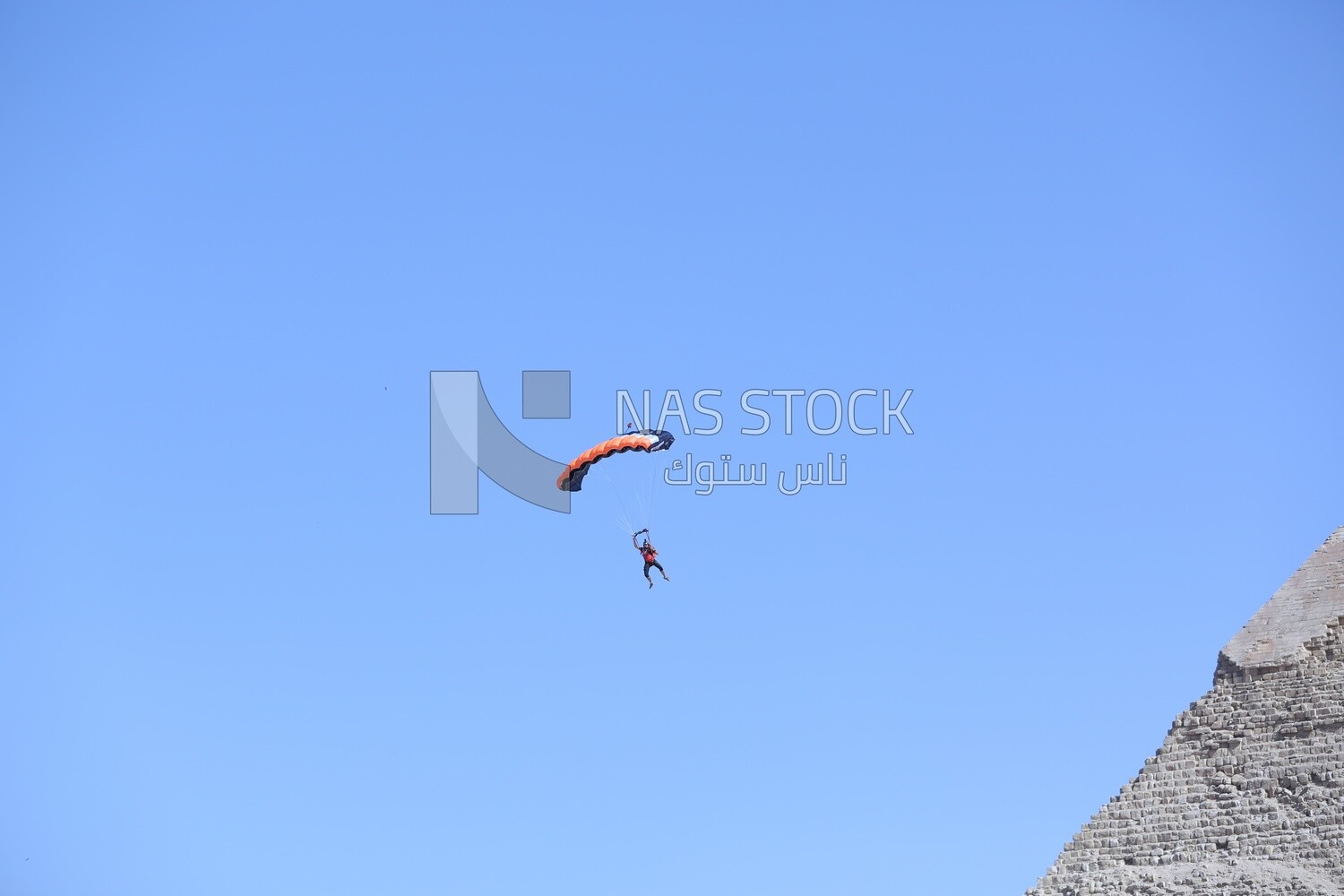 Scene of a person flying in the sky wearing a parachute in front of the Egyptian pyramids