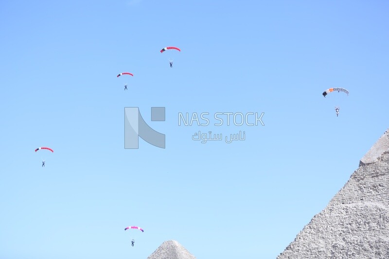 Person flying in the sky wearing a parachute in front of the Egyptian pyramids