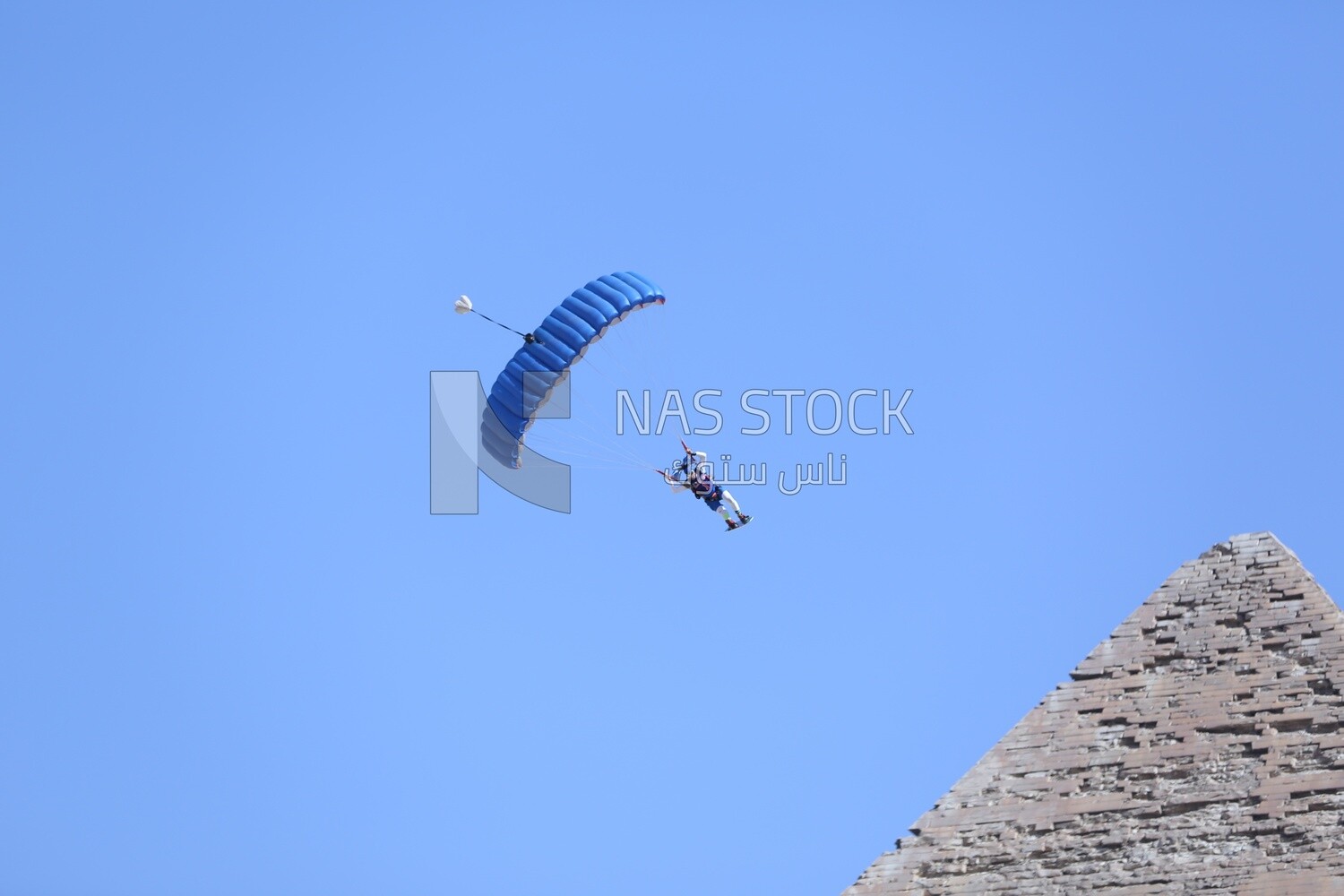 Scene of a person flying in the sky wearing a parachute in front of the Egyptian pyramids