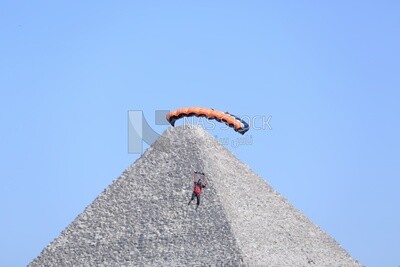 Scene of a person flying in the sky wearing a parachute in front of the Egyptian pyramids
