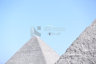 Person flying in the sky wearing a parachute in front of the Egyptian pyramids