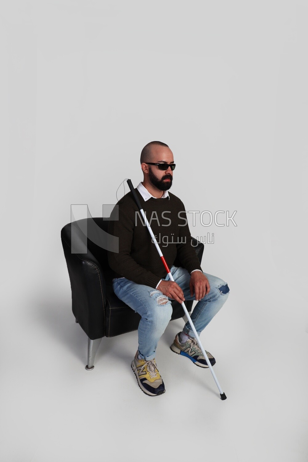 blind man sitting on a chair, wearing glasses and holding a walking stick