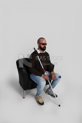 blind man sitting on a chair, wearing glasses and holding a walking stick