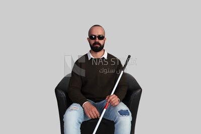 blind man sitting on a chair, wearing glasses and holding a walking stick