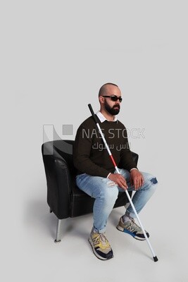 blind man sitting on a chair, wearing glasses and holding a walking stick