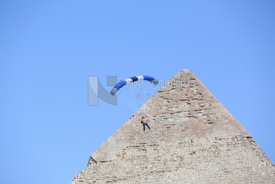 A person flying in the sky wearing a parachute in front of the Egyptian pyramids