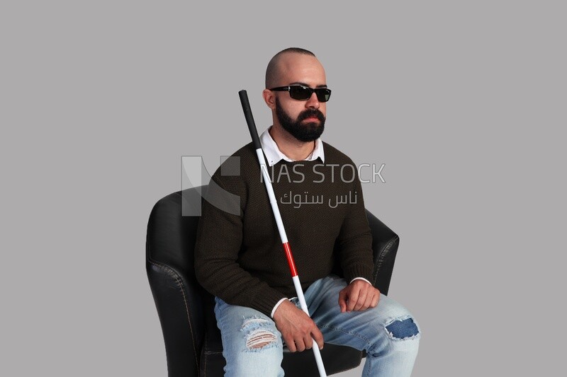 blind man wearing glasses and sitting on a chair with a walking stick