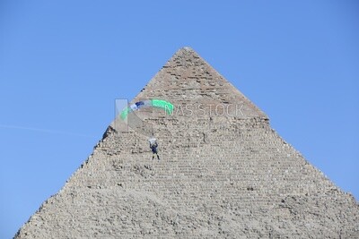 A person flying in the sky wearing a parachute in front of the Egyptian pyramids