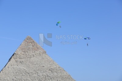 People flying in the sky wearing a parachutes over the Egyptian pyramids