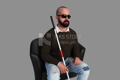 blind man wearing glasses and sitting on a chair with a walking stick