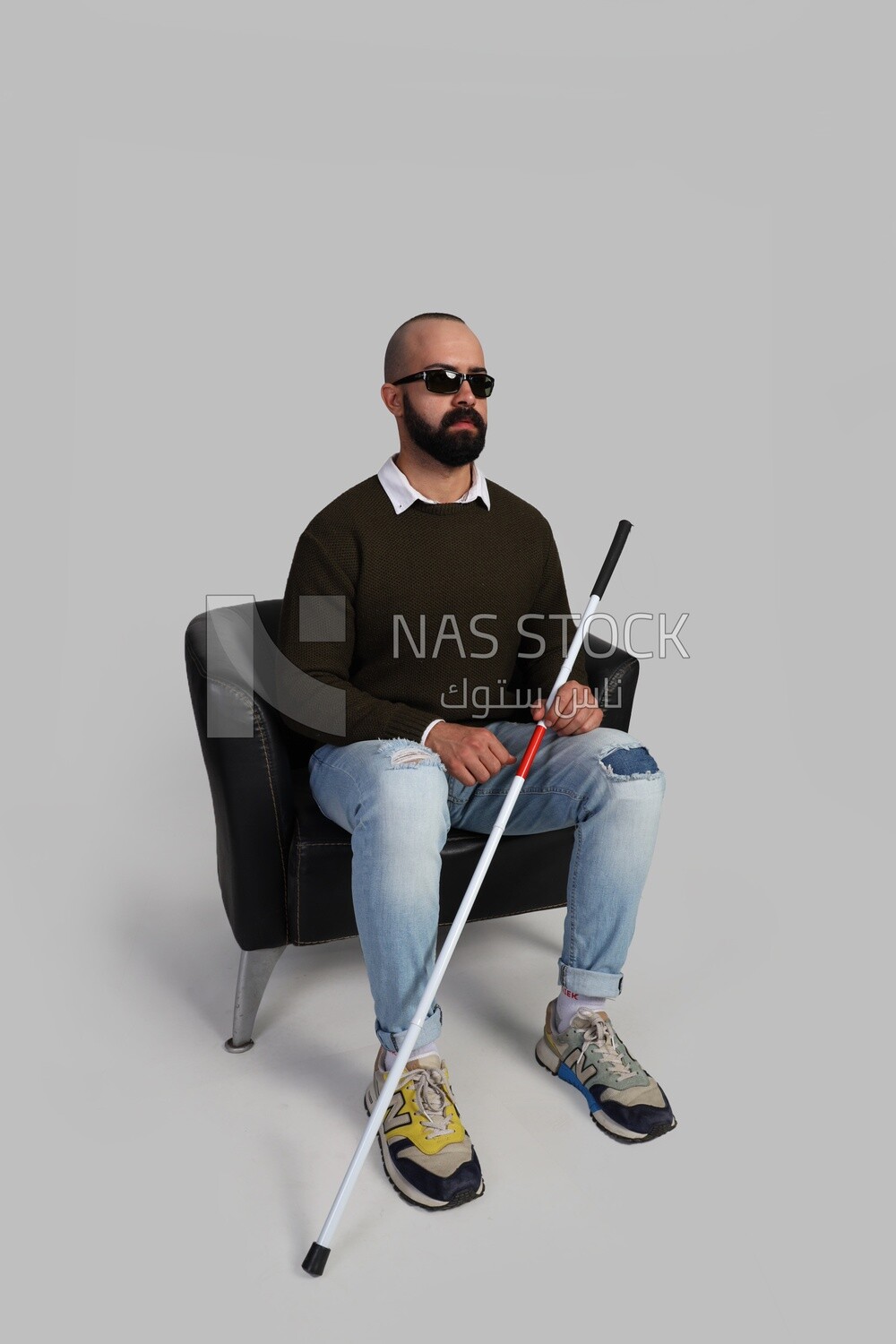 blind man wearing glasses and sitting on a chair with a walking stick