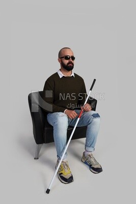 blind man wearing glasses and sitting on a chair with a walking stick