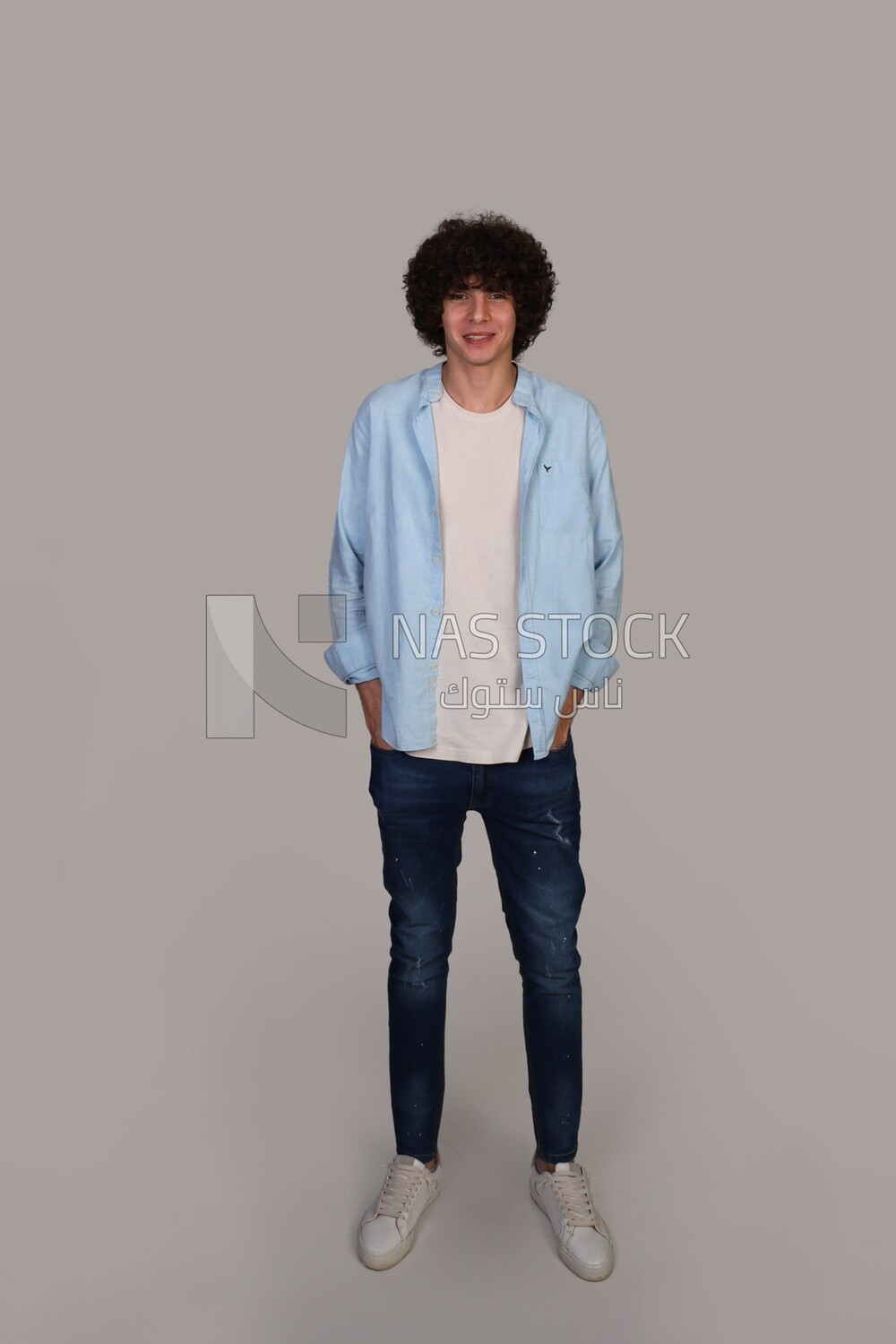young man with curly hair, wearing a shirt and putting his hand in his pocket