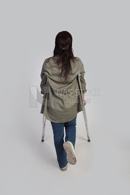 back view of a young woman with an injured leg walking with crutches, patient, medicine and health care concept, medical professions and jobs.