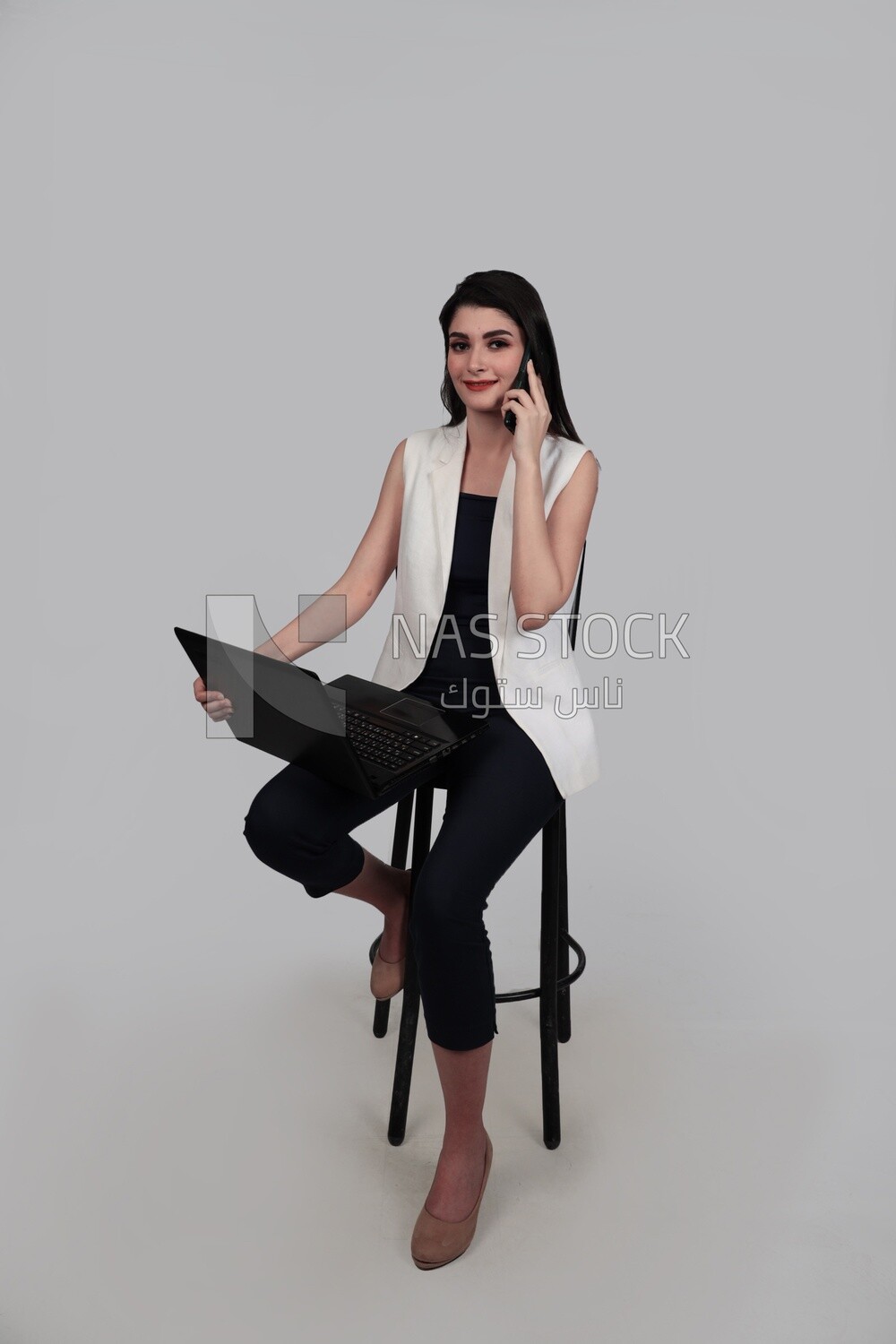 Photo of a businesswoman with formal wear sitting on a chair working on a laptop while talking on the phone, business development and partnerships, business meeting, Model