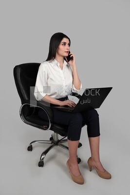 Photo of a businesswoman with formal wear sitting on a chair working on a laptop while talking on the phone, business development and partnerships, business meeting, Model