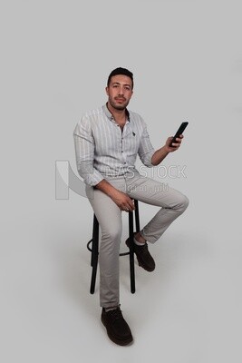 Photo Of a Handsome man sitting on a chair checking his mobile, Smiling Man, Wearing Casual Clothes Posing In a Light Room Interior, Smiling At the Camera, looking away