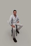 Photo Of a Handsome man sitting on a chair, Smiling Man, Wearing Casual Clothes Posing In a Light Room Interior, Smiling At the Camera, looking away