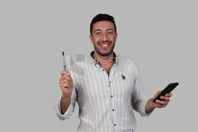 Photo Of a Handsome man standing looks thinking and checking his mobile, Smiling Man, Wearing Casual Clothes Posing In a Light Room Interior, Smiling At the Camera, looking away