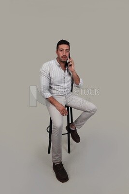 Photo Of a Handsome man sitting on a chair talking on his mobile, Smiling Man, Wearing Casual Clothes Posing In a Light Room Interior, Smiling At the Camera, looking away