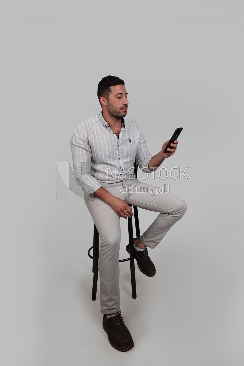 Photo Of a Handsome man sitting on a chair checking his mobile, Smiling Man, Wearing Casual Clothes Posing In a Light Room Interior, Smiling At the Camera, looking away