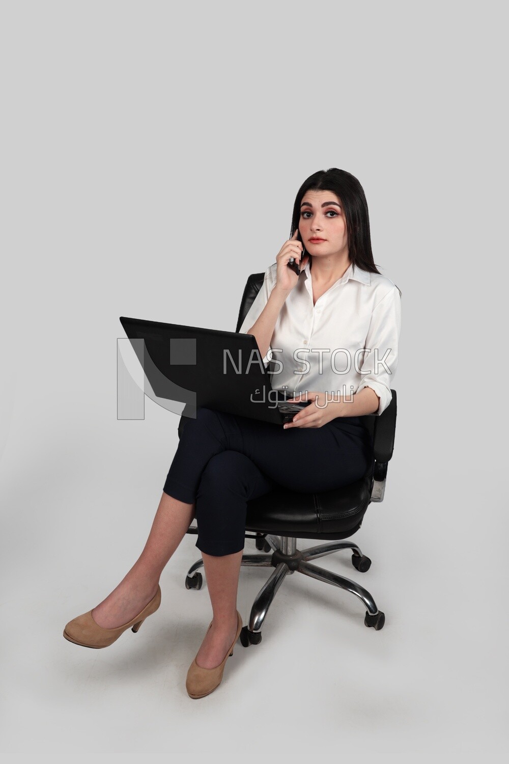 Photo of a businesswoman with formal wear sitting on a chair working on a laptop while talking on the phone, business development and partnerships, business meeting, Model