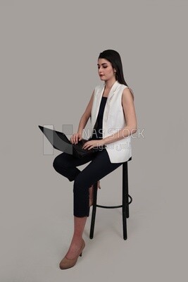 Photo of a businesswoman with formal wear sitting on a chair working on a laptop, business development and partnerships, business meeting, Model
