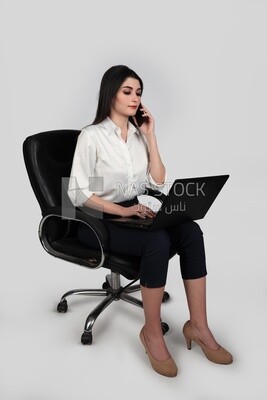 Photo of a businesswoman with formal wear sitting on a chair working on a laptop while talking on the phone, business development and partnerships, business meeting, Model