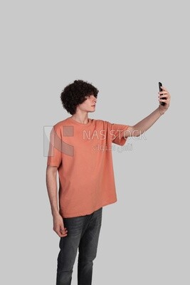 مراهق بشعر مجعد وملابس صيفية يلتقط صورة سيلفى