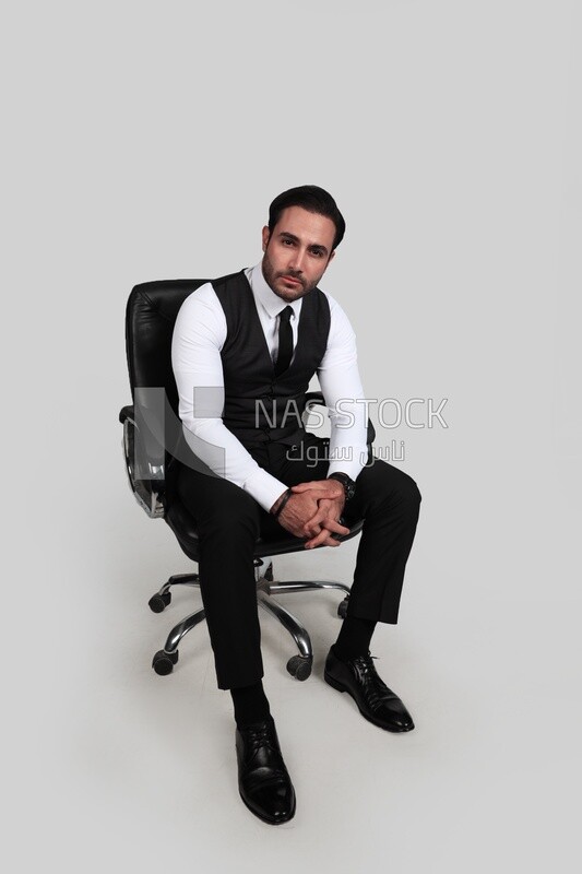 Photo of a businessman with a formal suit sitting on a chair and looking at the camera, business development and partnerships, business meeting, Model