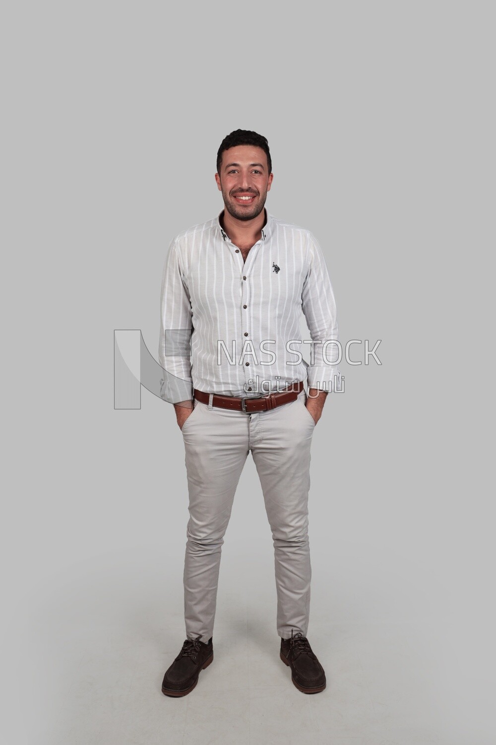 Photo Of a Handsome man standing and putting his hands in his pocket, Smiling Man, Wearing Casual Clothes Posing In a Light Room Interior, Smiling At the Camera, looking away