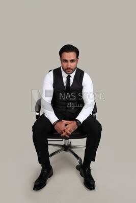 Photo of a businessman with a formal suit sitting on a chair and looking at the camera, business development and partnerships, business meeting, Model
