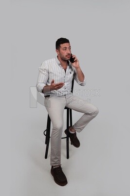 Photo Of a Handsome man sitting on a chair talking on his mobile, Smiling Man, Wearing Casual Clothes Posing In a Light Room Interior, Smiling At the Camera, looking away