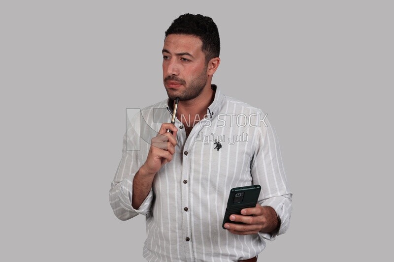 Photo Of a Handsome man standing and checking his mobile, Smiling Man, Wearing Casual Clothes Posing In a Light Room Interior, Smiling At the Camera, looking away