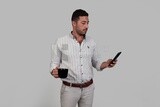 Photo Of a Handsome man holding his mobile in one hand and a cup in the other, Smiling Man, Wearing Casual Clothes Posing In a Light Room Interior, Smiling At the Camera, looking away