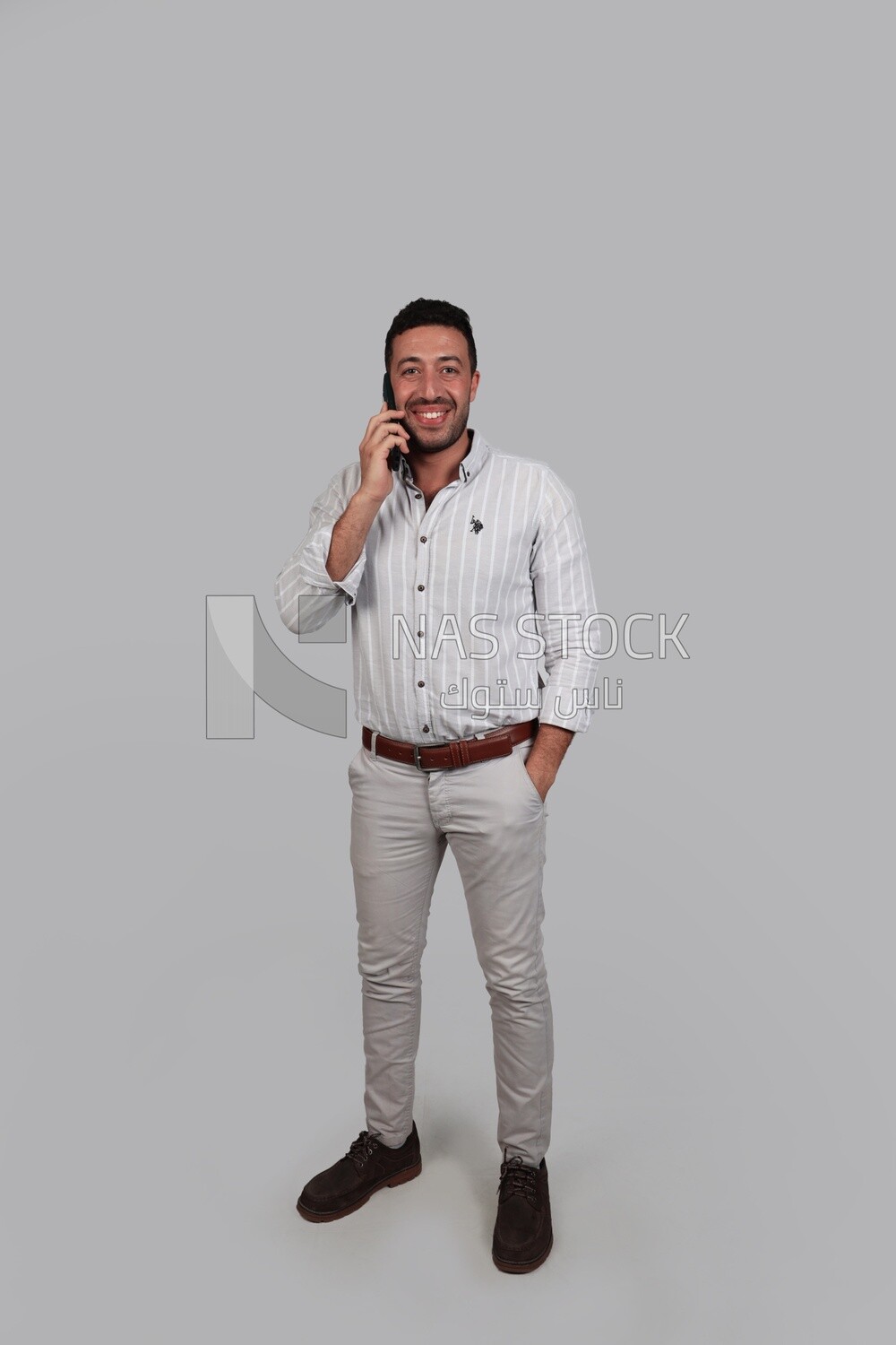 Photo Of a Handsome man standing and talking on his phone, Smiling Man, Wearing Casual Clothes Posing In a Light Room Interior, Smiling At the Camera, looking away