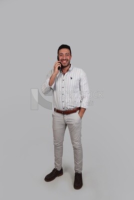 Photo Of a Handsome man standing and talking on his phone, Smiling Man, Wearing Casual Clothes Posing In a Light Room Interior, Smiling At the Camera, looking away